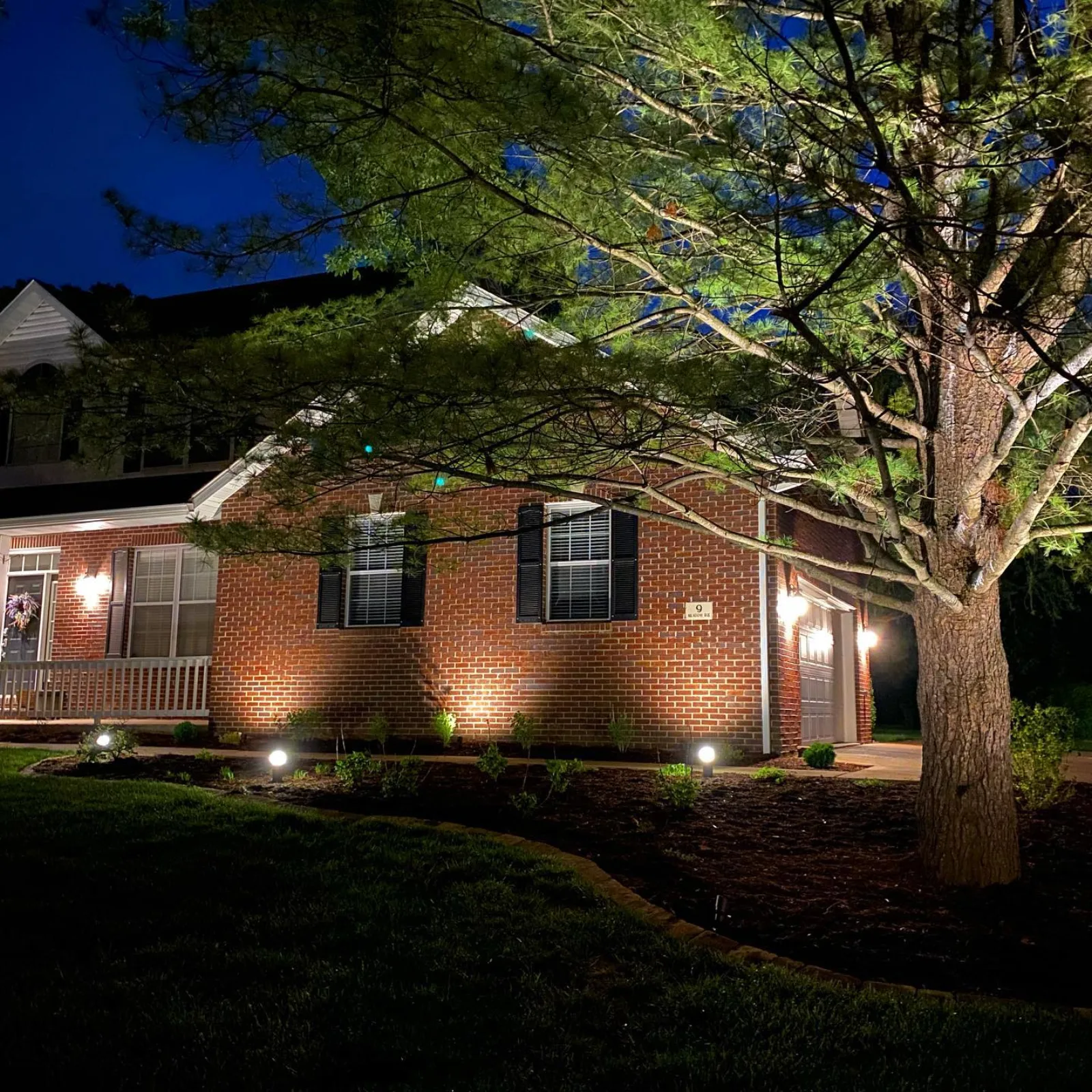 Landscape lighting washing a brick home and mature pine at night
